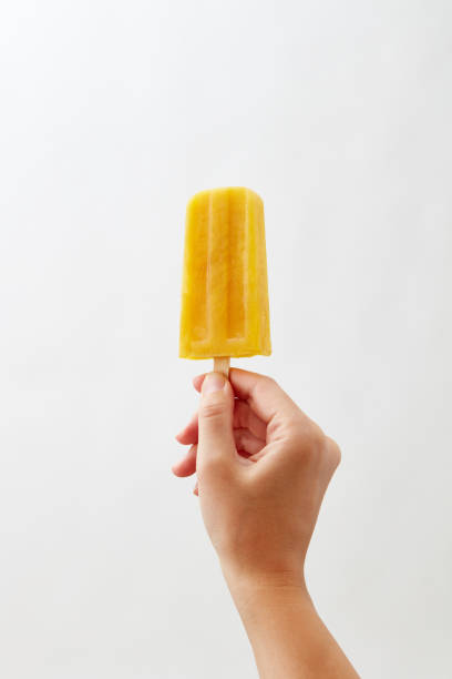 istock A woman's hand holds a yellow yoghurt ice cream lolly on a white background with copy space. Healthy food. Business concept concept 1030164036