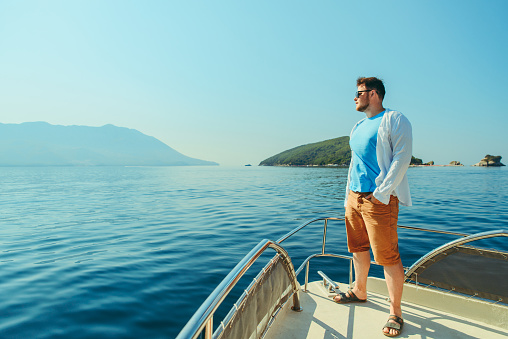 success man standing at nose of boat with sea and mountains on background. summer vacation