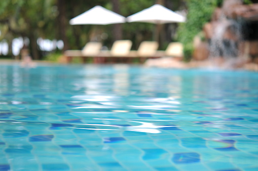 Stone podium stand in luxury blue pool water. Summer background of tropical design product placement display. Hotel resort poolside backdrop.