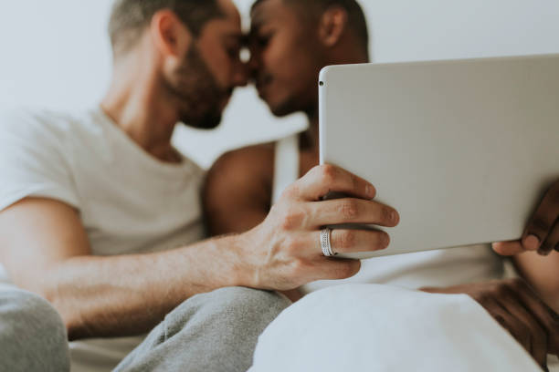 coppia gay che usa un tablet a letto - couple black american culture kissing foto e immagini stock