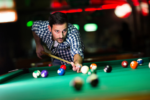 Young attractive man playing pool in bar alone