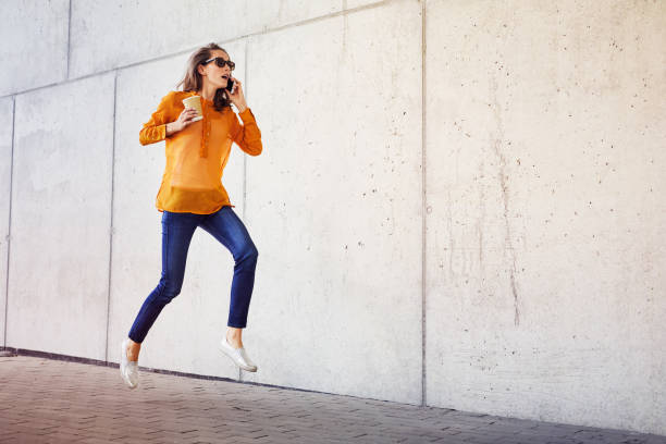 Young woman talking on phone and drinking coffee while rushing to work