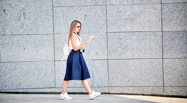 istock Young woman with digital camera using tablet PC while walking outdoors in city street 1030228024