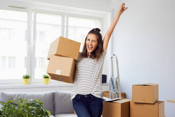 Joyful young woman standing in new apartment with arm raised after moving in stock photo
