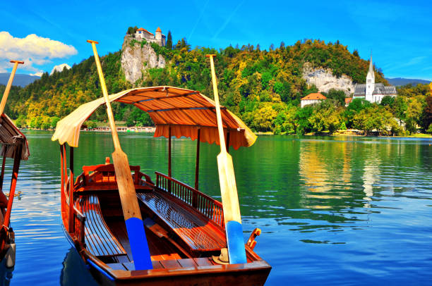 tradizionale barca pletna sul lago di bled. una barca che trasporta turisti sull'isola dove si trova la chiesa assunzione di maria. sullo sfondo si trova il famoso vecchio castello sulla scogliera. slovenia - santa maria church foto e immagini stock