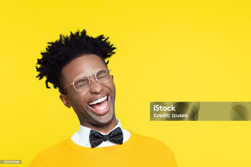 Funny portrait of nerdy young man laughing with eyes closed Funny portrait of happy nerdy young afro American man wearing yellow sweater and black bow tie laughing with eyes closed. Comedian Stock Photo