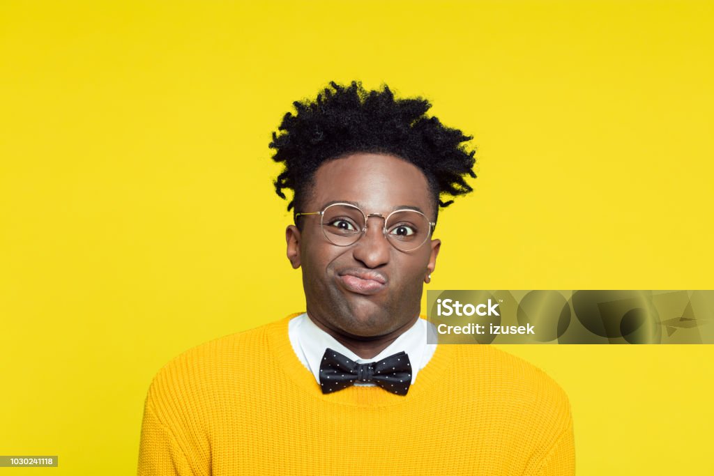 Portrait of disgusted geeky young man in retro style against yellow background Portrait of displeased nerdy young afro american man wearing yellow sweater and black bow tie standing against yellow background. 1980-1989 Stock Photo