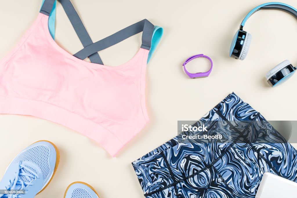 Woman sport bra, leggins, sneakers, headphones and fitness tracker on neutral background. Sport fashion concept. Woman sport bra, leggins, sneakers and fitness tracker on neutral background. Sport fashion concept. Flat lay, top view Flat Lay Stock Photo