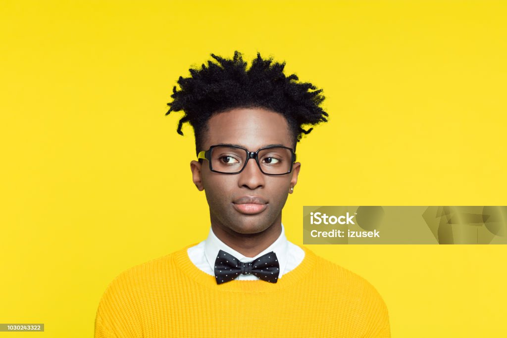 Funny portrait of smiling nerdy young man in retro style Funny portrait of nerdy young afro American man wearing yellow sweater and glasses, looking away. Nerd Stock Photo