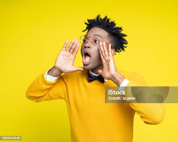 Portrait Of Nerdy Young Man Shouting Against Yellow Background Stock Photo - Download Image Now