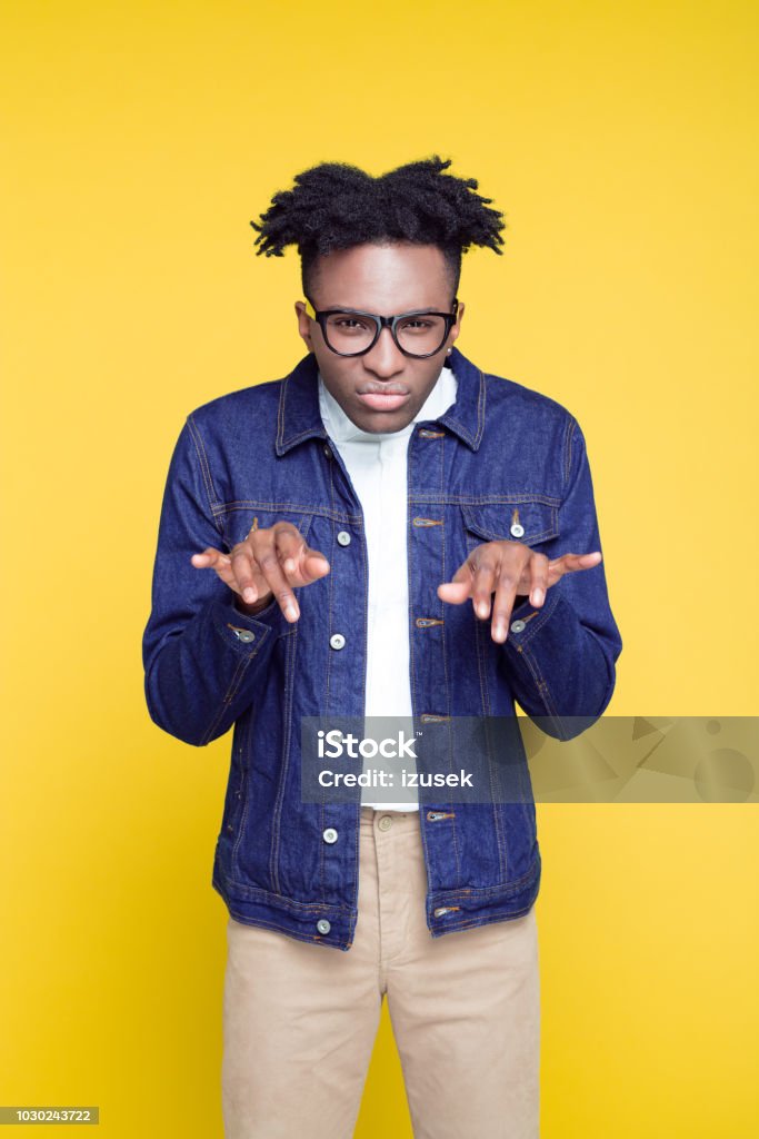 80's style portrait of confident nerdy young man Portrait of nerdy young afro American man wearing oversized jeans jacket and glasses, standing against yellow background. 1980-1989 Stock Photo