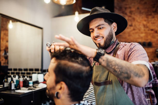 barbiere sorridente che taglia i capelli del cliente in salone - negozio del barbiere foto e immagini stock