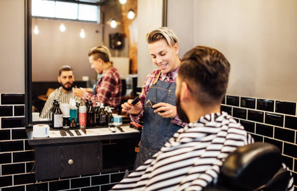 Female hairdresser with tools by customer in salon Female hairdresser with electric razor and hairbrush by customer. Young barber is preparing for a haircut for the client. They are at hair salon. salon mirror stock pictures, royalty-free photos & images