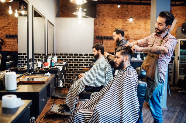 Hairdressers cutting hair of clients in salon Hairdressers cutting hair of clients. Professional barbers are giving new look to customers. They are in barber shop. barber shop stock pictures, royalty-free photos & images