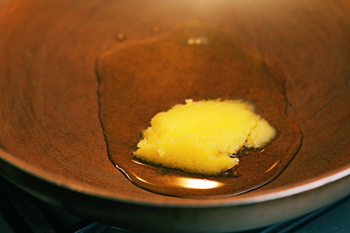 High-angle look at ghee (clarified butter) melting in a frying pan ready to saute something.