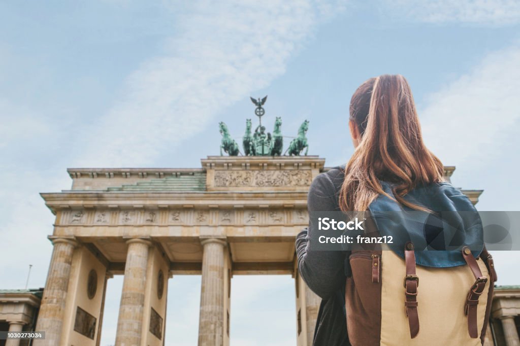 Una turista con uno zaino che guarda la Porta di Brandeburgo a Berlino - Foto stock royalty-free di Germania