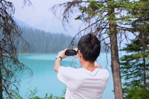 A man using his phone to take a photo of Emerald Lake in the Canadian Rockies.
