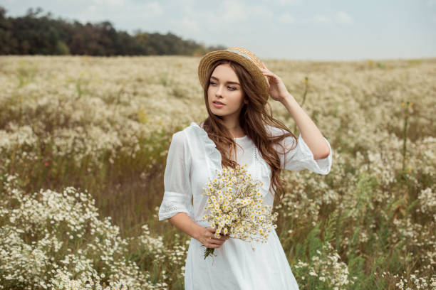 草原の野生のカモミールの花の花束と白いドレスでかなり物思いにふける女性の肖像 - floral dress ストックフォトと画像