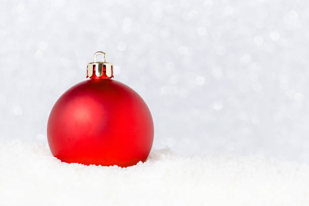 christmas red bauble in snow on white background with bokeh, selective focus