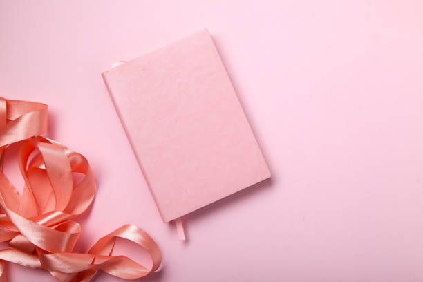 istock Pink notebook with shiny pink satin ribbon on pink background. Monochromatic concept. 1030288624