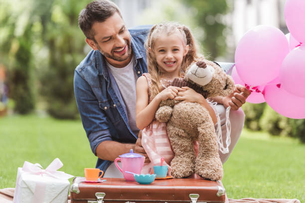istock father and daughter with teddy bear playing tea party at lawn 1030294768