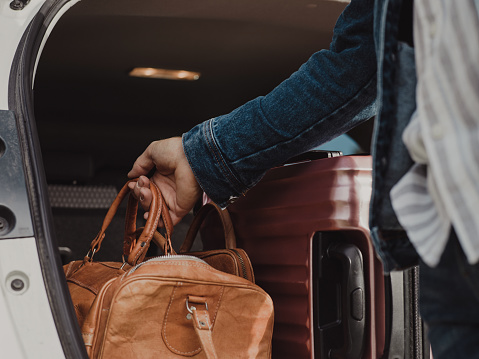 Man packing in his luggage suitcase in his car ready for road trip\nPhoto taken outdoors of man with bags by his Station wagon