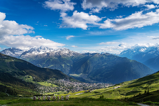 Scenery view of Verbier village surrounded with beautiful Swiss Alps mountains in sunny summer day with green meadows, forests, blue sky.