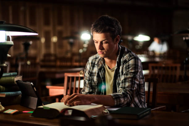 young man reading in library at night - old fashioned desk student book imagens e fotografias de stock