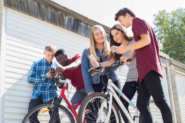 grupo de amigos adolescentes em bicicletas olhando para telefones móveis - text messaging mobile phone teenagers only people - fotografias e filmes do acervo