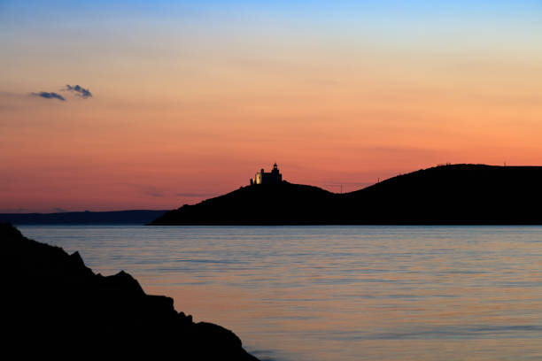 View on water surface and mountain silhouette with lighthouse at pink sunset
