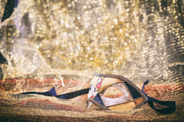 Close up of ball and details of golden Venetian mask, fancy carnival mask on golden surface.