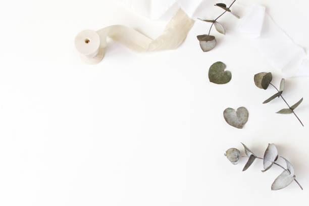 Feminine wedding desktop scene. Composition of dry silver dollar eucalyptus leaves and silk ribbons on white table background. Flat lay, top view.