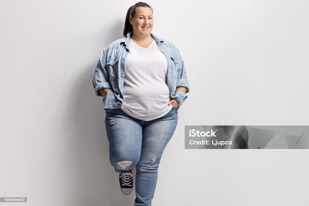 Young overweight woman standing against a wall Young overweight woman in casual clothes standing against a wall Overweight Stock Photo