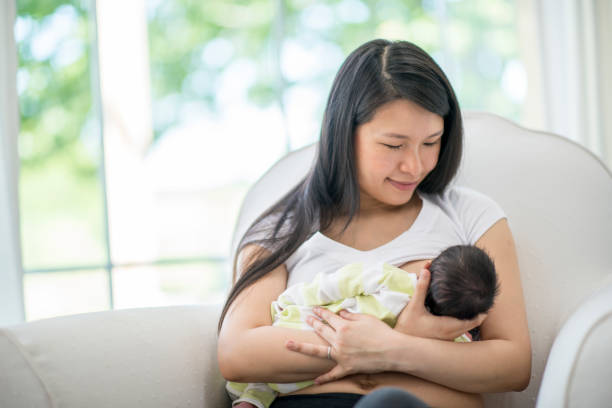 Breastfeeding Mother A mother and newborn baby boy are indoors in their house. The mother is breastfeeding her son while sitting in a chair. breastfeeding photos stock pictures, royalty-free photos & images