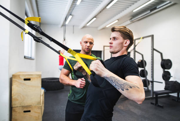 istock Fit young man with a personal trainer in gym doing exercise with TRX. 1030361648