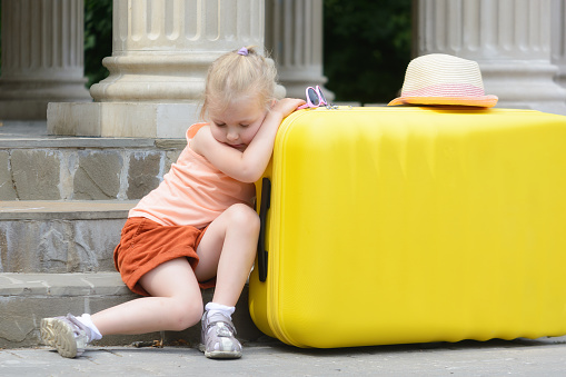 The little girl fell asleep, leaning her elbows on a big yellow suitcase. Portrait of a pretty girl. T