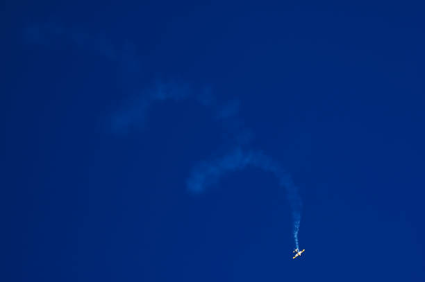 avion acrobatique avec trail blanc spirale de fumée sur le ciel bleu - airplane stunt yellow flying photos et images de collection