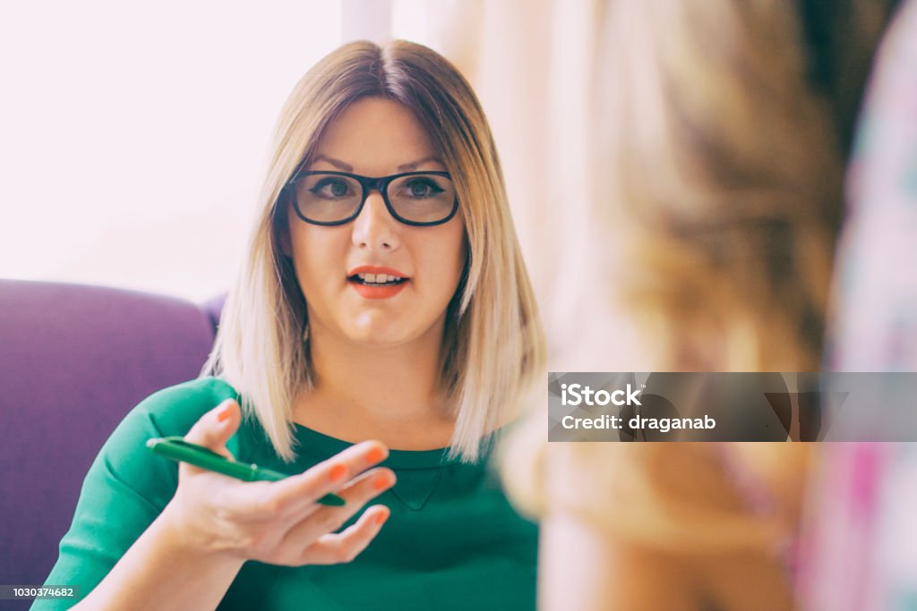 Female counselor talks with a client Portrait of young woman talking to an unrecognized person who sits across her Discussion Stock Photo