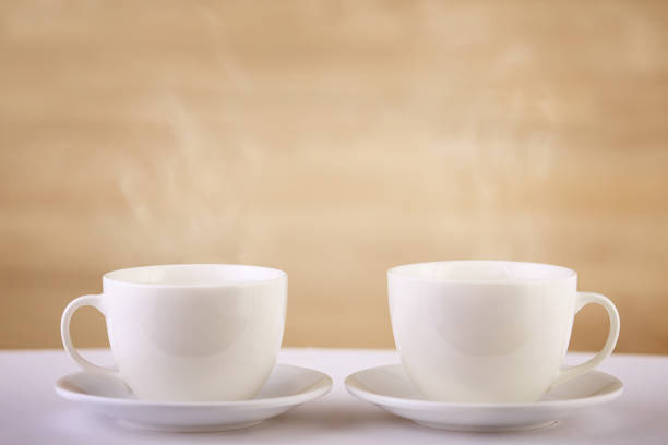 Two white porcelain teacups on white table over beige background show clean and simple design ideas. Selective focus, shallow depth of field, close-up. Studio shot. Pure design concept. Stylish elements.