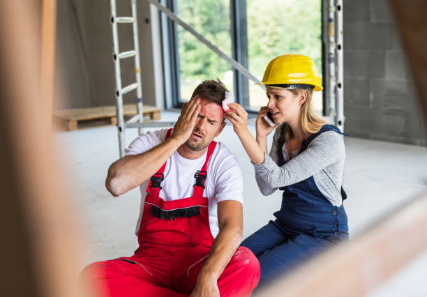 una mujer con el teléfono inteligente ayuda a trabajador del hombre después de un accidente en el sitio de construcción. - accident occupation physical injury construction fotografías e imágenes de stock