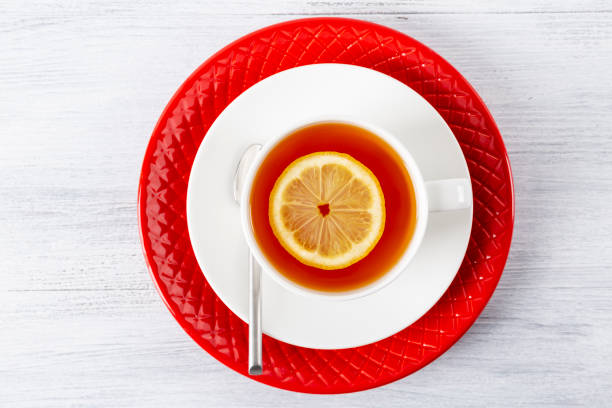 istock Tea with lemon in a white mug on a red plate. On a wooden table. Tea spoon. Top view. Copy space. 1030383532