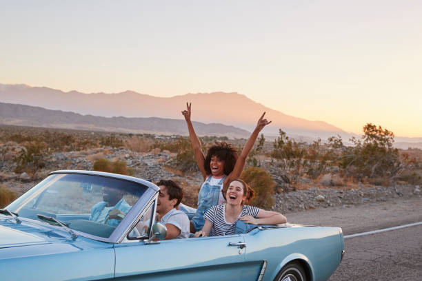 group of friends on road trip driving classic convertible car - american holiday imagens e fotografias de stock