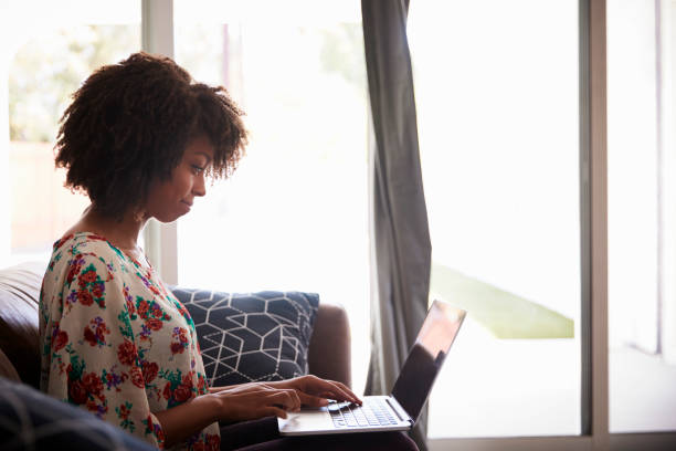 istock Side View Of Woman Sitting On Sofa At Home Using Laptop 1030408558