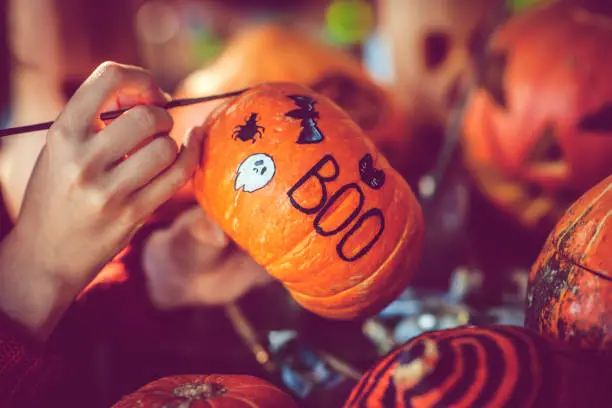 Photo of Young girl painting on pumpkin in Halloween