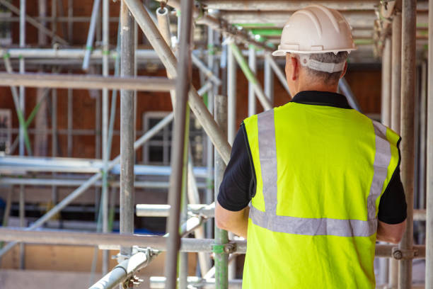 Rear view of male builder construction worker on building site wearing hard hat and hi-vis vest stock photo