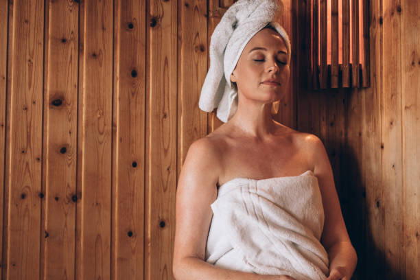 Woman sitting in a spa with eyes closed Woman with towel wrapped around her body and head sitting in sauna spa peacefully. Woman relaxing in a wooden spa with eyes closed. woman wrapped in bath towel stock pictures, royalty-free photos & images