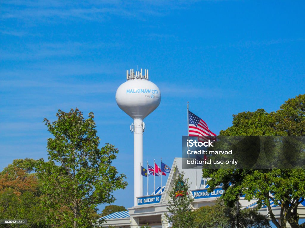 Water-tower, american flag and green trees. Summer view with blue sky on sunny day. MACKINAW CITY, MICHIGAN, USA - September 23,  2017. American Flag Stock Photo