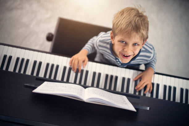 Overhead shot of little boy playing piano. The boy is 8 years old and is sitting by modern digital piano.\nNikon D850