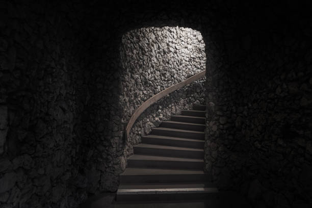 Old dark cellar made from small pieces of stone and staircase towards the exit and light.