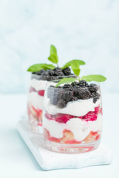 Two dairy dessert with blueberries, cherries, corn flakes and cheese, spoon, napkin, blueberries and cherries on a wooden board